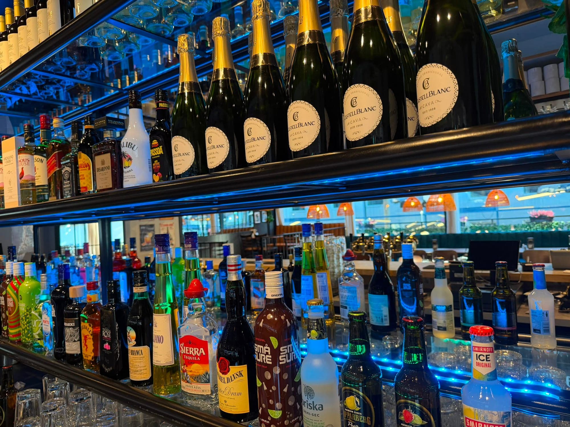 Flaskhyllan bakom baren med cava och sprit i blått ljus